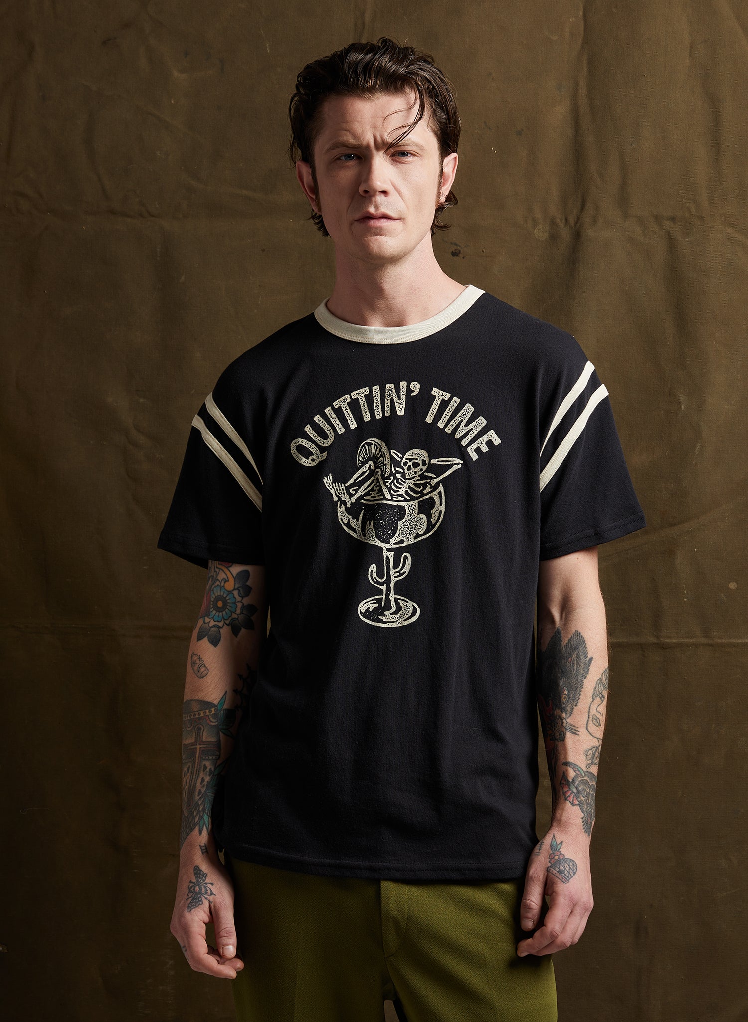 Model wearing Pyknic Quittin' Time Tee in Black, showcasing snarky skeleton margarita print and bold contrasting stripes.