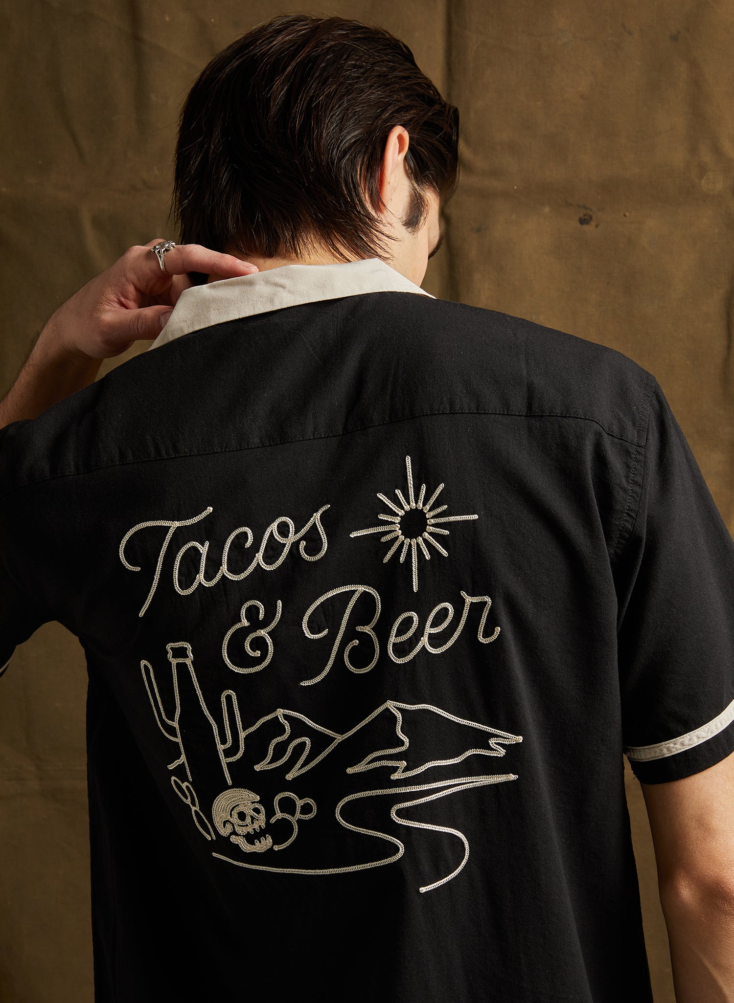 Back view of male model in black Tacos and Beer Button-Up Shirt with cream collar and chainstitch embroidery